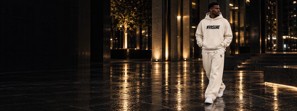 NVRSAME Bone Shift — cremefarbener Oversized Hoodie und weite Pants auf einer beleuchteten Plaza bei Nacht